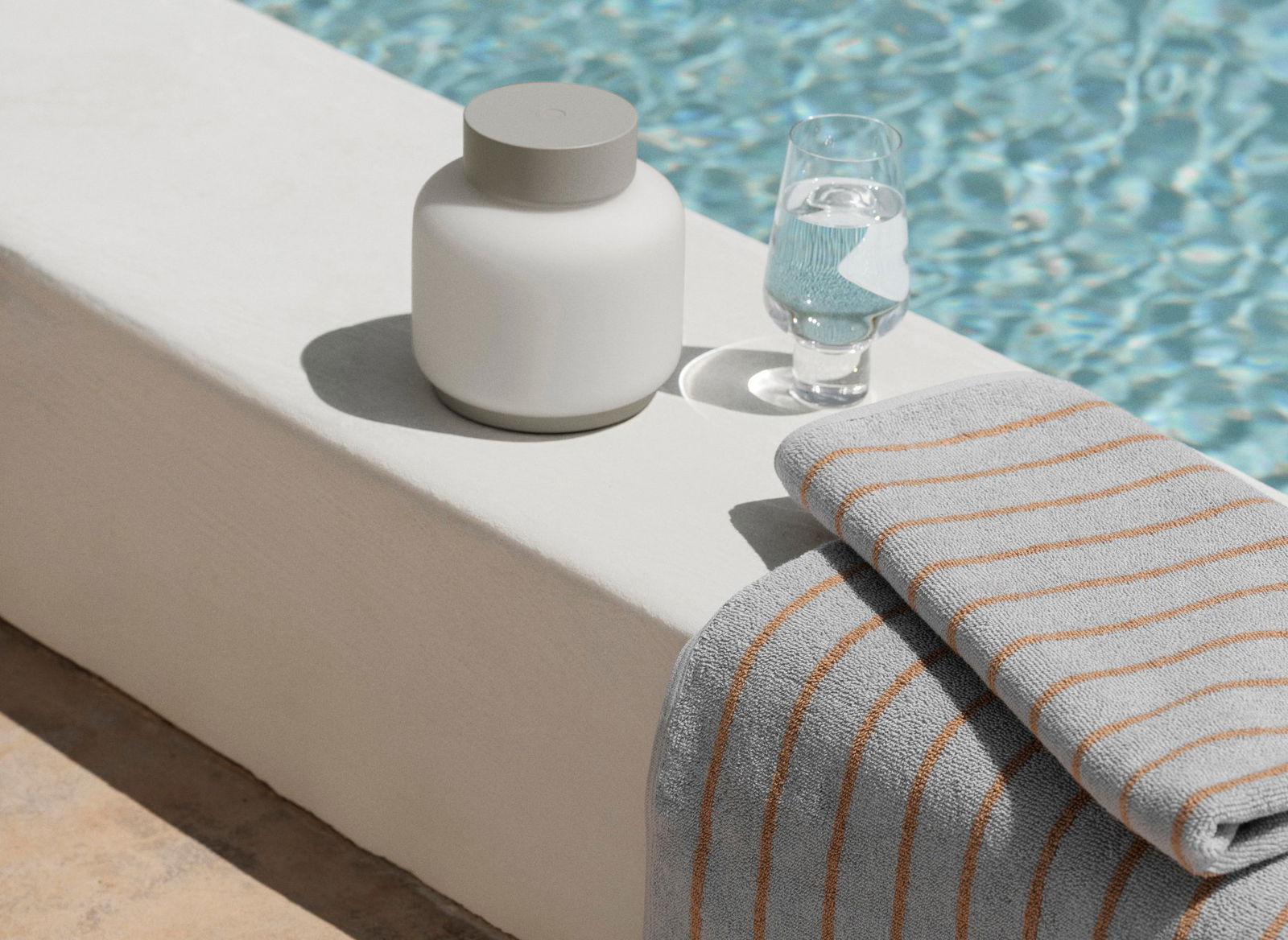 Elegante Poollandschaft mit einem weißen Behälter, einem Glas Wasser und einem gestreiften Handtuch.