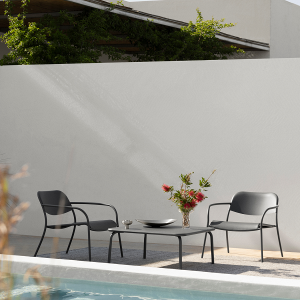 Moderner Außenbereich mit schwarzen Stühlen, einem Tisch und einer Blumenvasen neben einem Pool.
