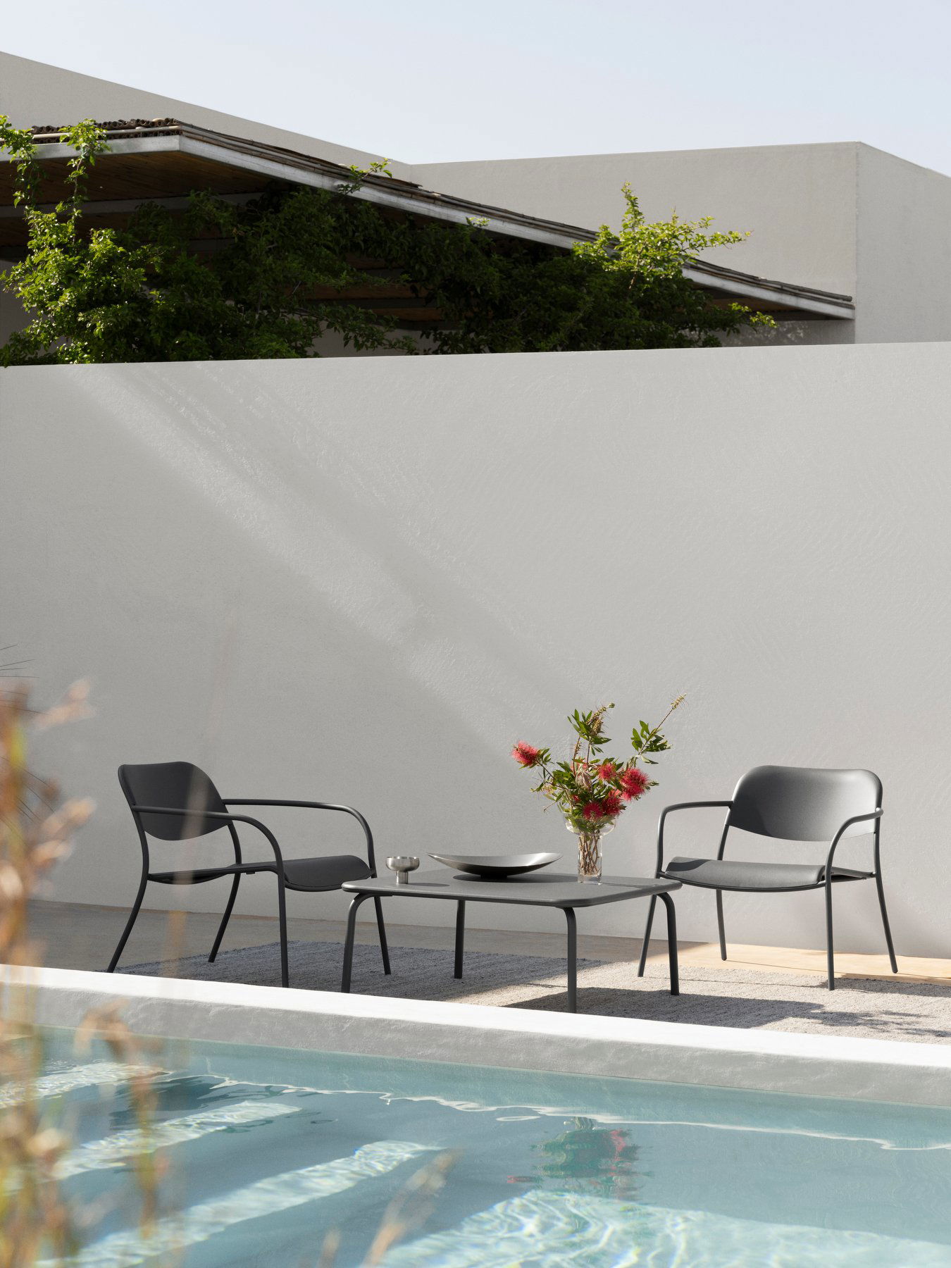 Moderner Außenbereich mit schwarzen Stühlen, einem Tisch und einer Blumenvasen neben einem Pool.
