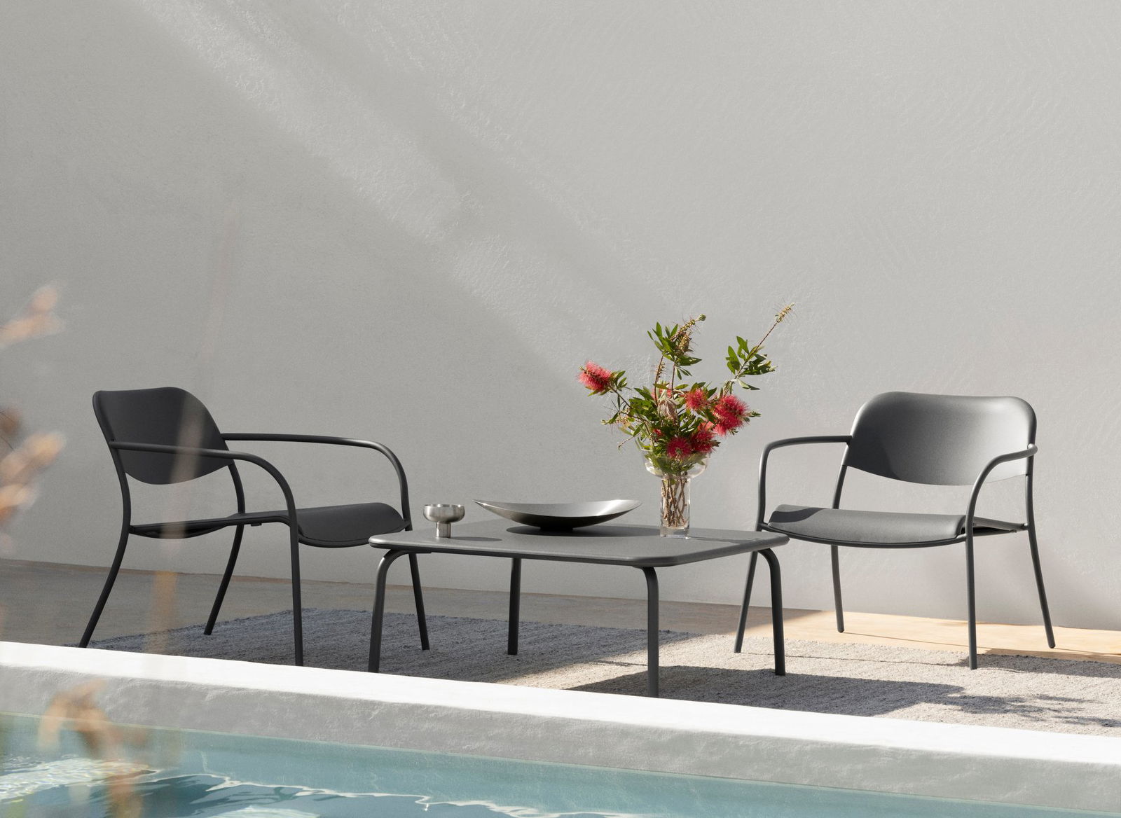 Stylischer Außenbereich mit Sitzgelegenheiten in der Nähe eines Pools, mit einer Vase mit Blumen auf einem Tisch.