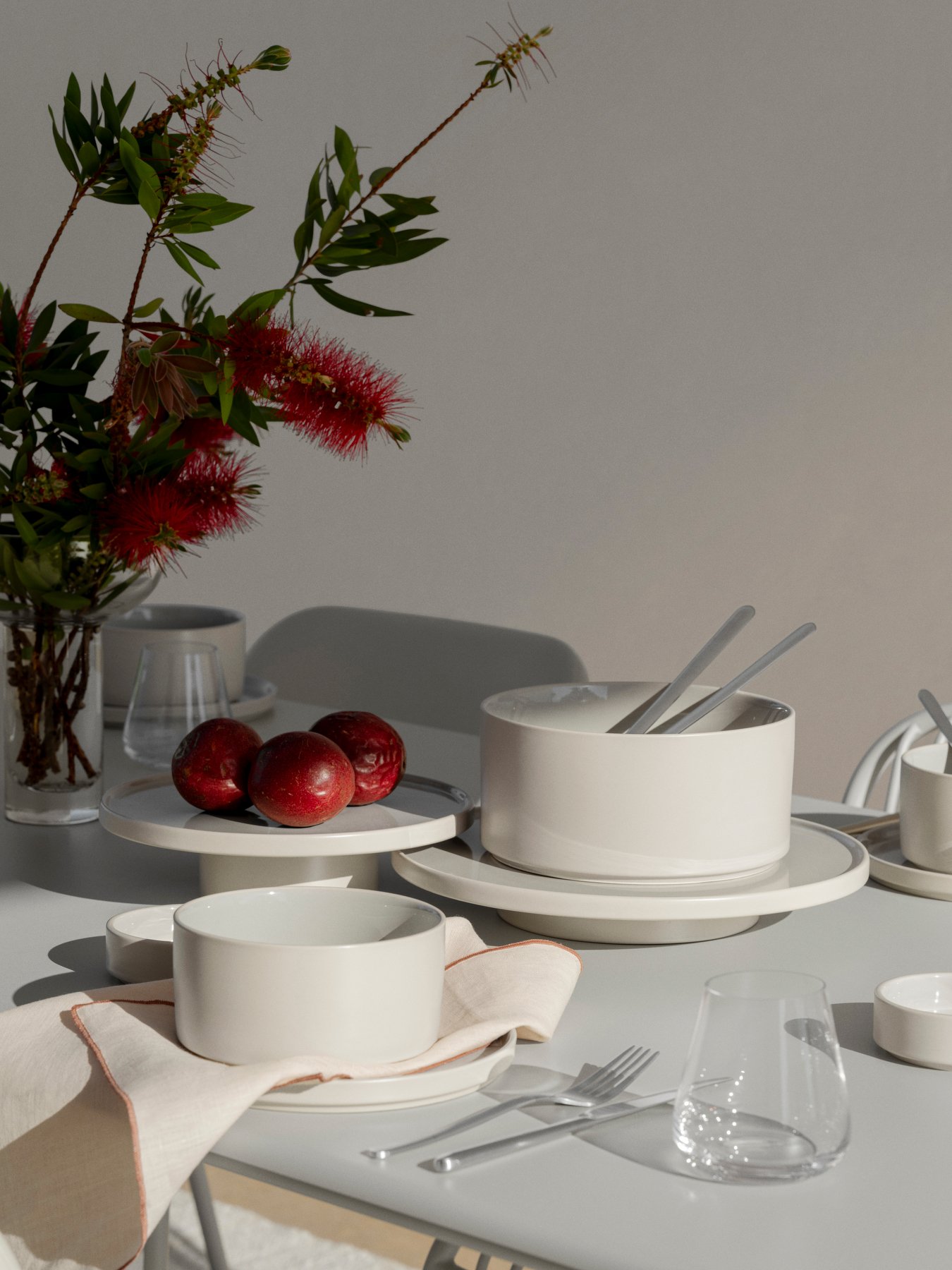 Elegante Tischdekoration mit weißem Geschirr, roten Äpfeln und frischen Blumen.
