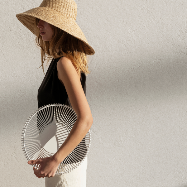 Woman wearing a straw hat holding a decorative white plate against a textured wall.