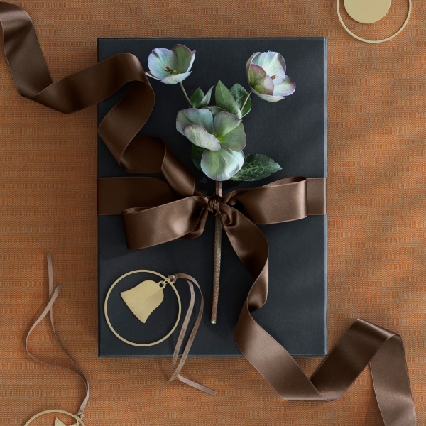 Elegant gift box adorned with a brown ribbon and a floral arrangement on a textured orange background.