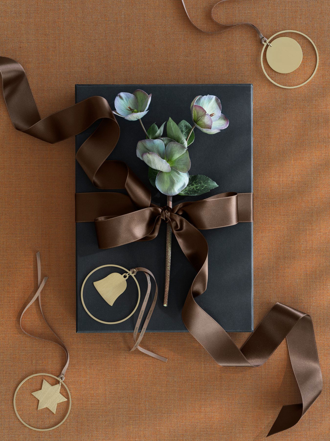 Elegant gift box adorned with a brown ribbon and a floral arrangement on a textured orange background.