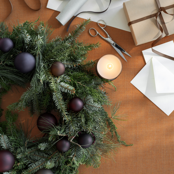 Festlicher Weihnachtskranz mit Ornamenten, Kerzen und Geschenken auf einem rustikalen Tisch.