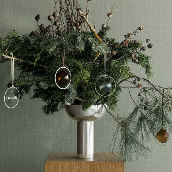 Festliche Grünpflanzenarrangement mit Glasornamenten in einer modernen Metallvase.