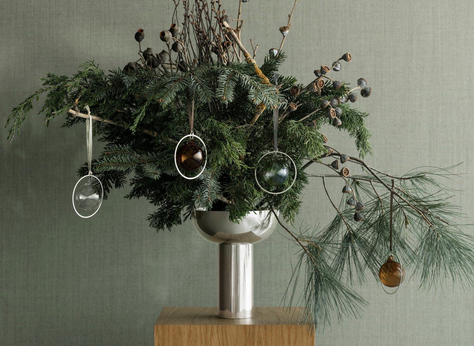 Festliche Grünpflanzenarrangement mit Glasornamenten in einer modernen Metallvase.