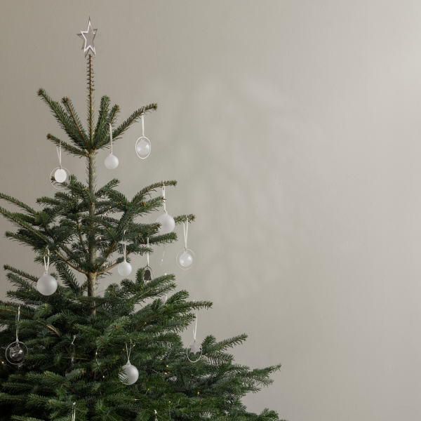 Minimalistischer Weihnachtsbaum mit Glasornamenten und einem Stern oben an einer neutralen Wand.