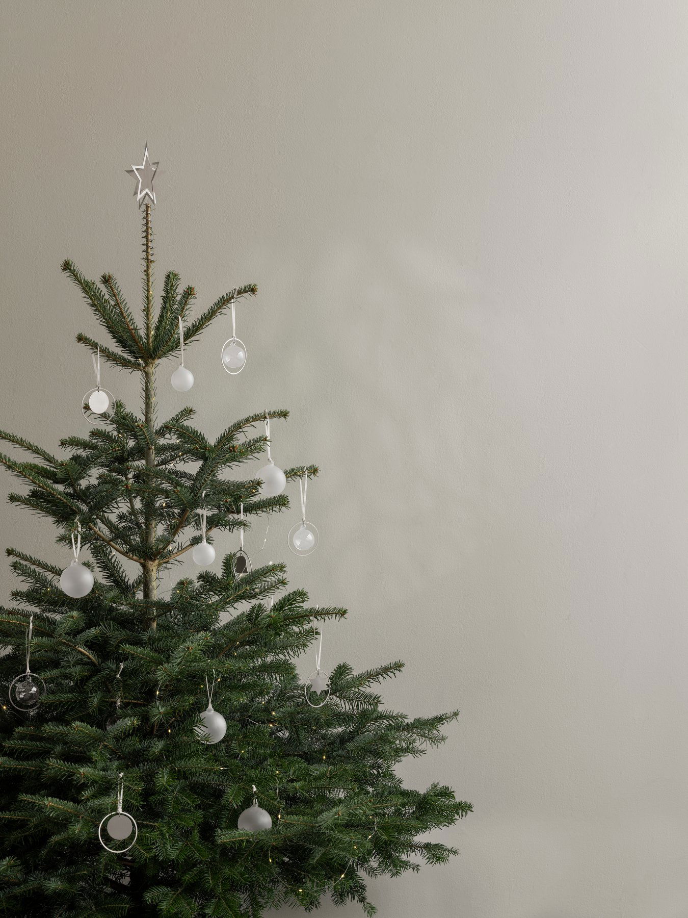 Minimalistischer Weihnachtsbaum mit Glasornamenten und einem Stern oben an einer neutralen Wand.