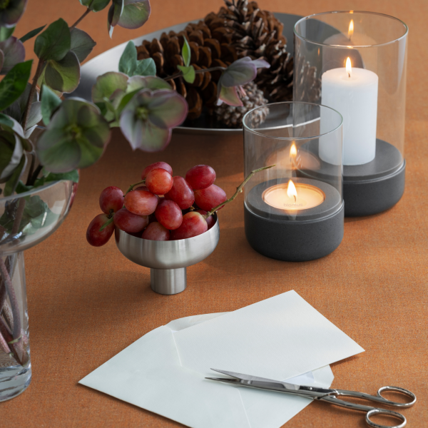 Stylische Tischdekoration mit Trauben, Kerzen und Tannenzapfen auf einer orangefarbenen Tischdecke.