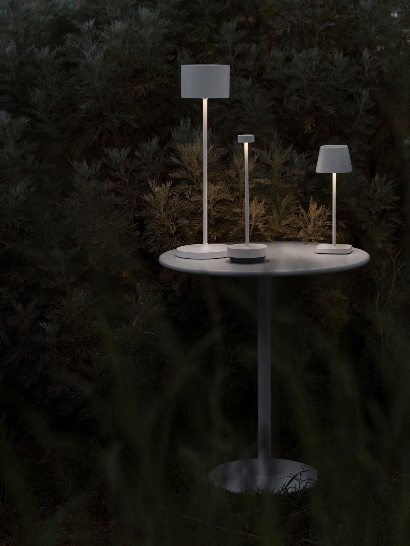 Moderne Außenlampen auf einem Tisch, umgeben von üppigem Grün bei Nacht.