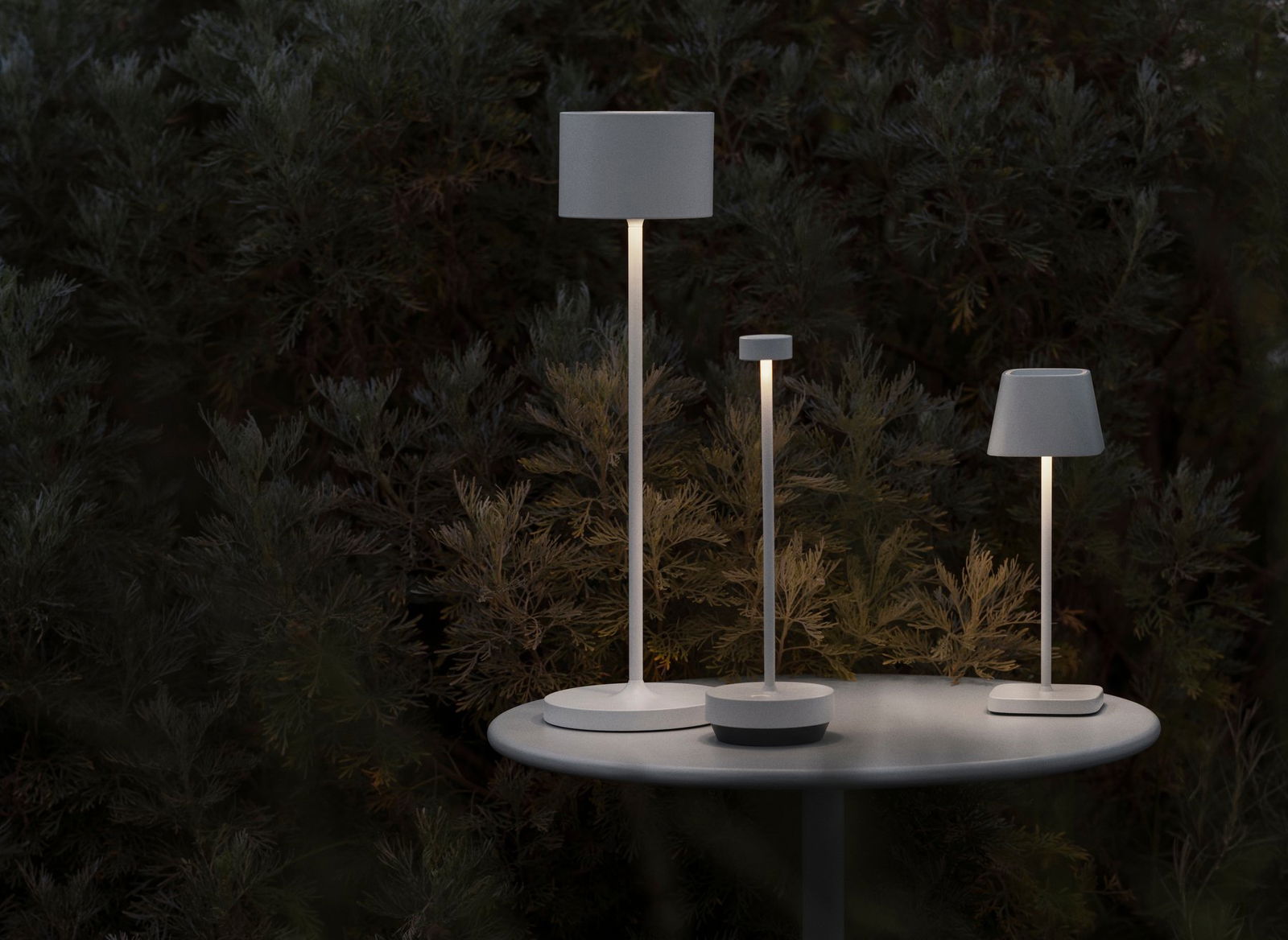 Moderne Außenlampen beleuchten einen Gartentisch inmitten üppiger Grünheiten bei Nacht.