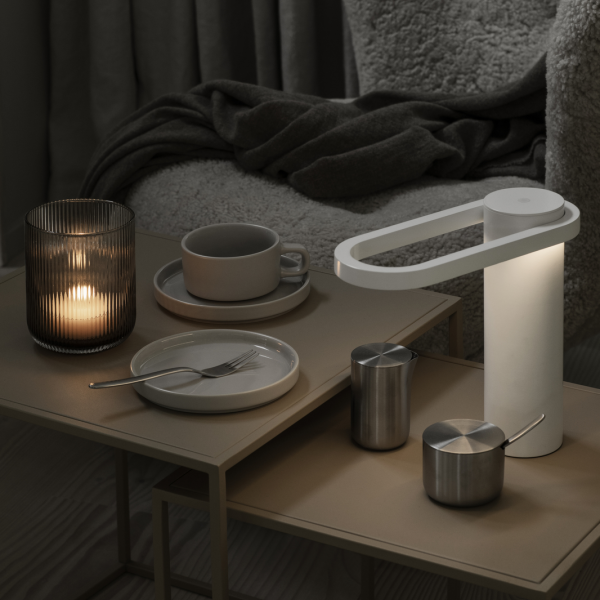 Moderne Tischdeko mit einer stilvollen Lampe, Kerze und minimalistischen Geschirr auf einer gemütlichen Oberfläche.