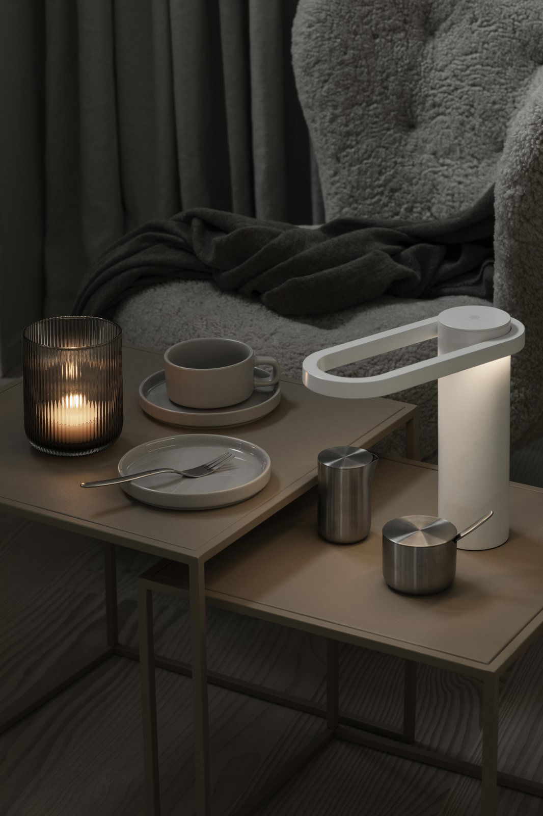 Moderne Tischdeko mit einer stilvollen Lampe, Kerze und minimalistischen Geschirr auf einer gemütlichen Oberfläche.