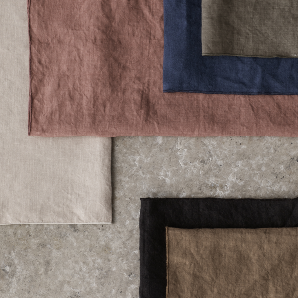 Piles of textured fabric swatches in neutral and earthy tones on a stone surface.