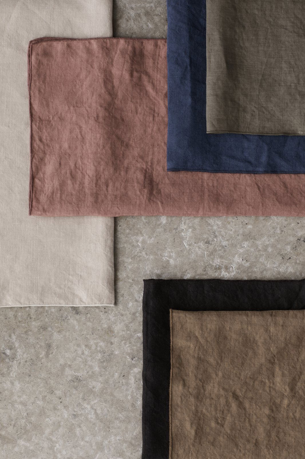 Piles of textured fabric swatches in neutral and earthy tones on a stone surface.
