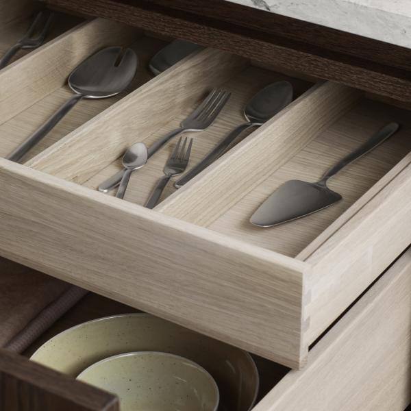 Organized kitchen drawer with stainless steel utensils and serving tools on a wooden interior.