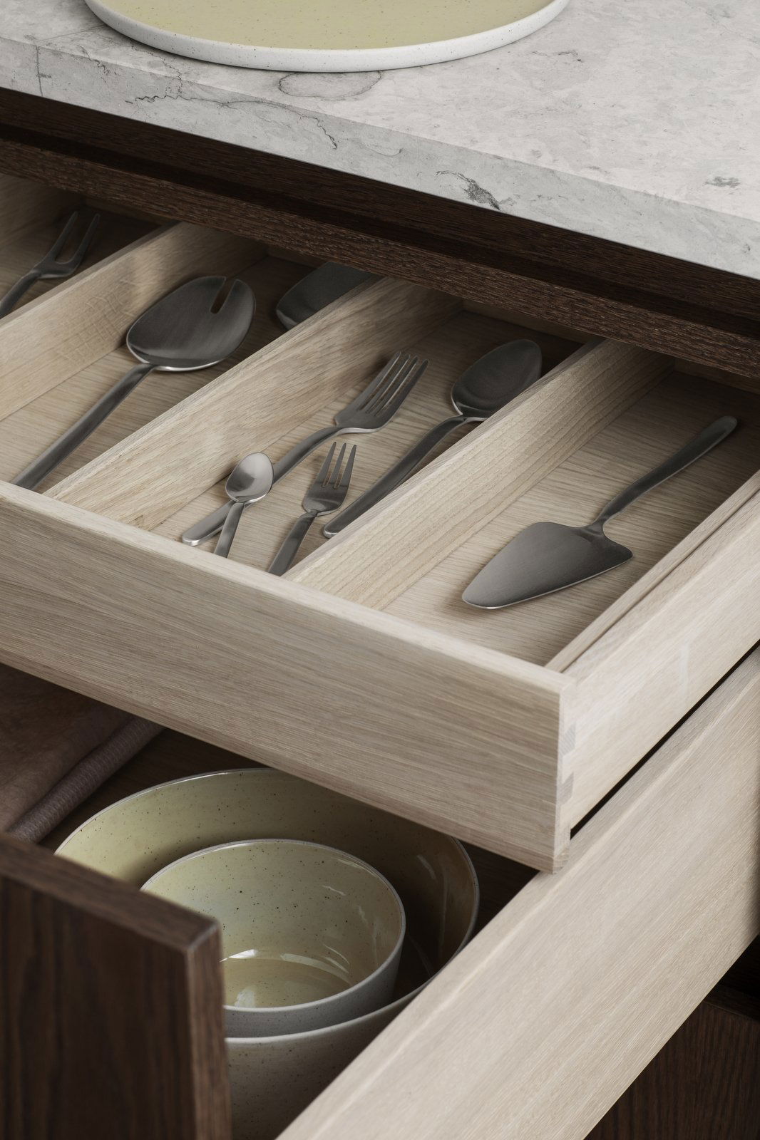 Organized kitchen drawer with stainless steel utensils and serving tools on a wooden interior.