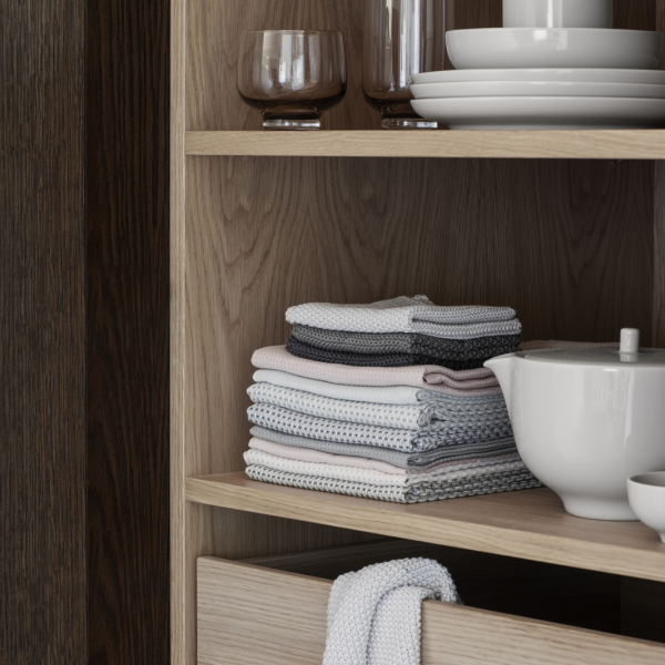 Neatly organized kitchen shelves featuring glassware, plates, and folded dishcloths.