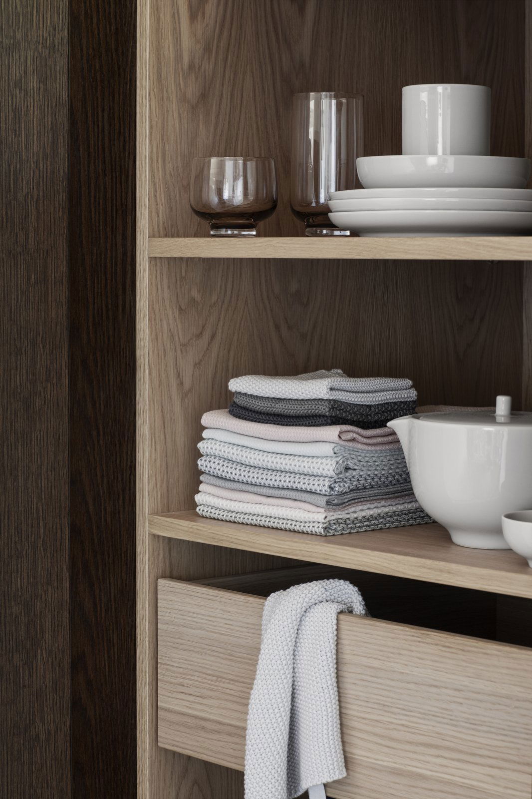 Neatly organized kitchen shelves featuring glassware, plates, and folded dishcloths.