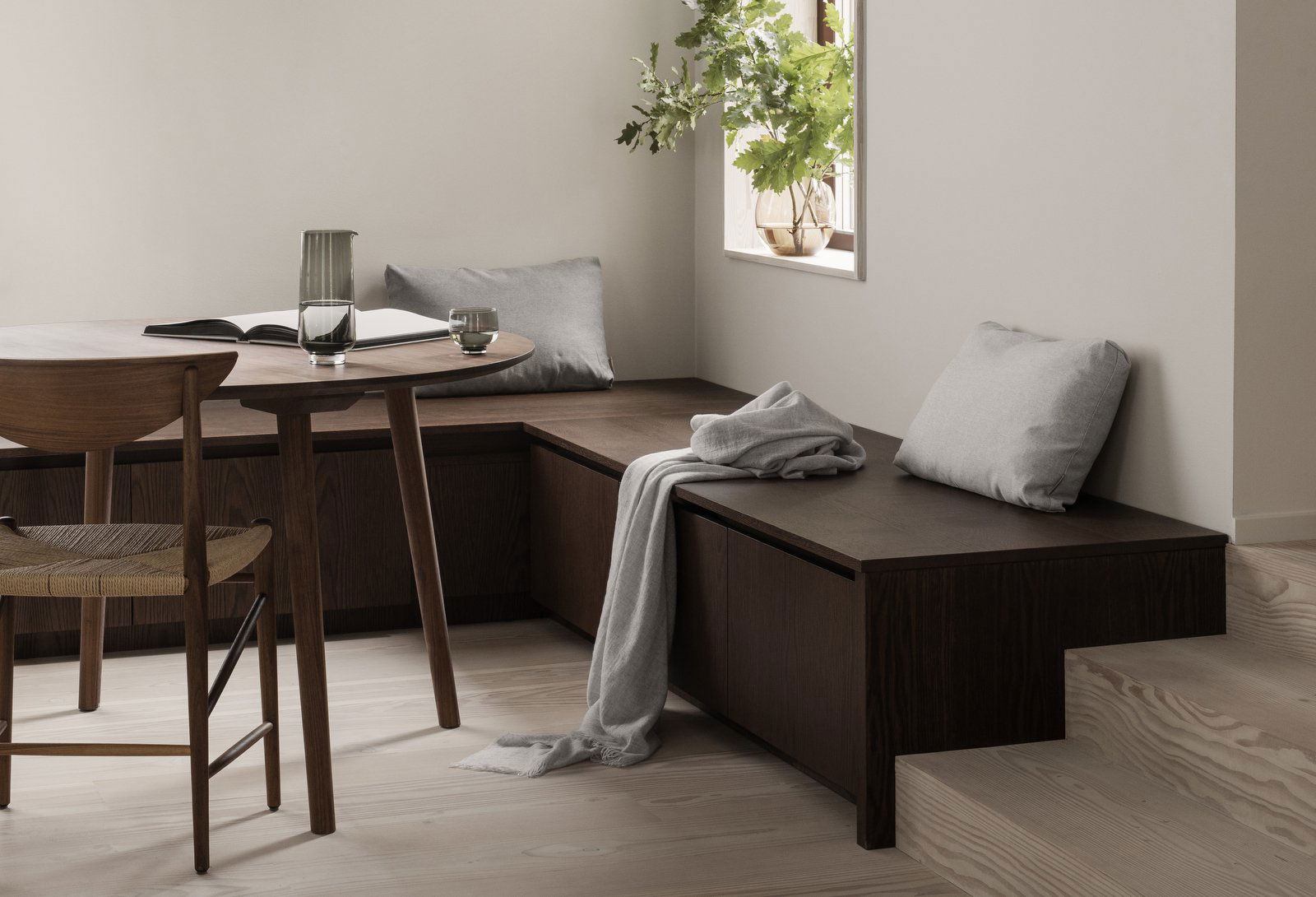 Gemütlicher minimalistischer Essbereich mit Holzsitzen, Kissen und einem Tisch am Fenster.
