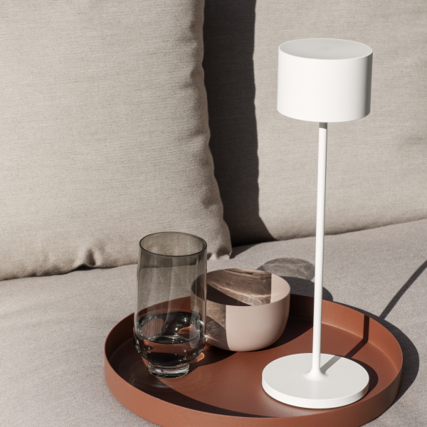 Modern lamp, glass, and bowl on a tray atop a stylish couch in natural light.