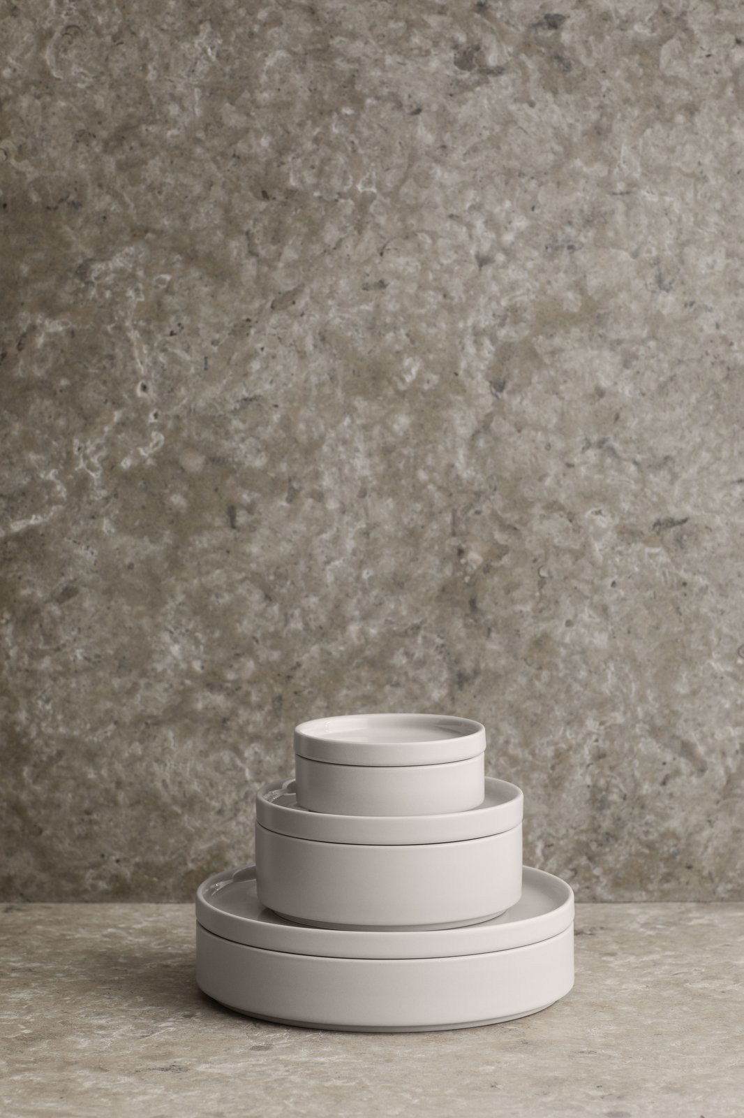 Minimalist white ceramic bowls stacked against a textured gray stone background.