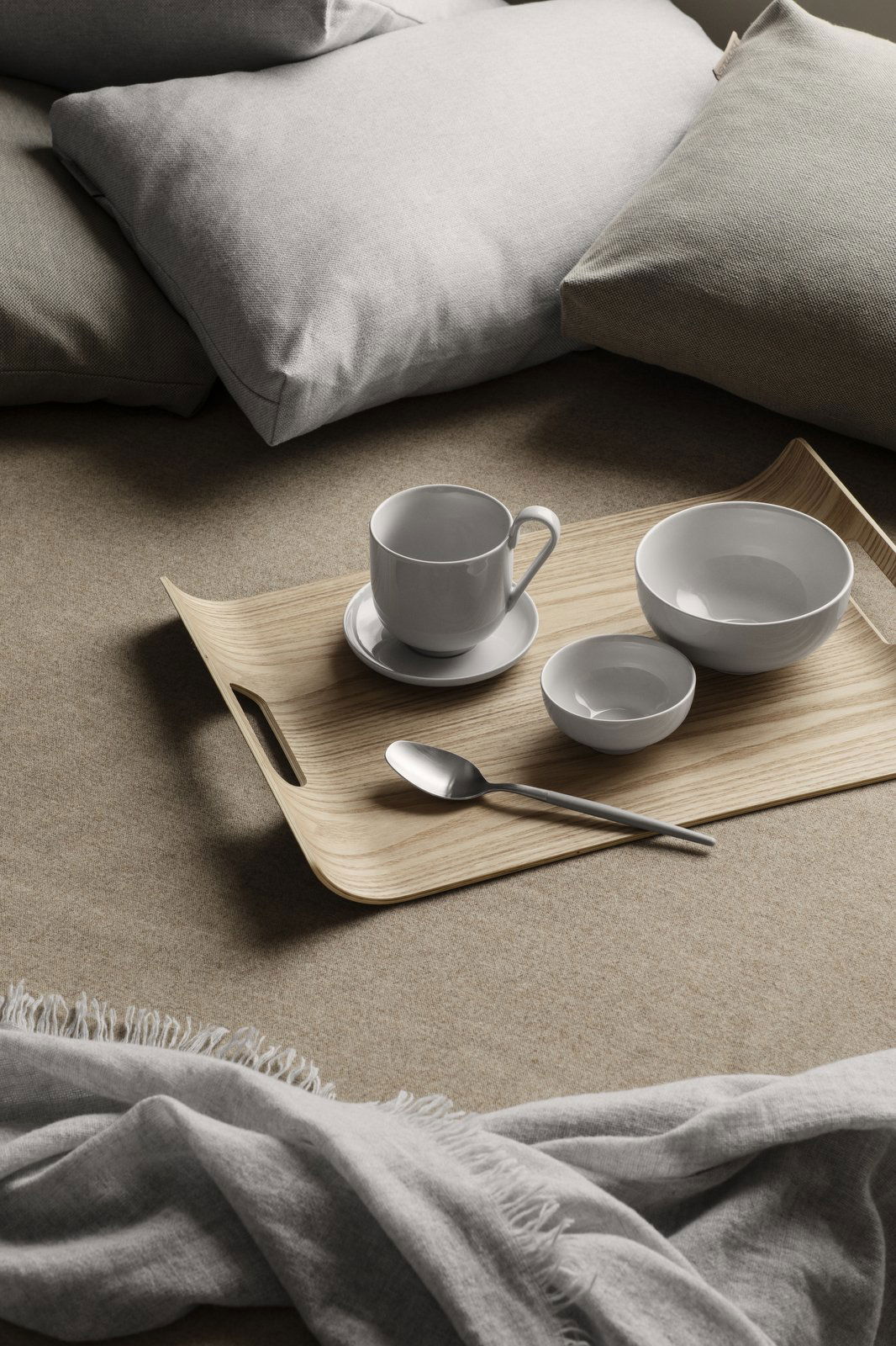 Elegant wooden tray with white dinnerware and a silver spoon on a cozy beige background.