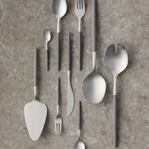 Modern stainless steel cutlery arranged on a textured gray surface.