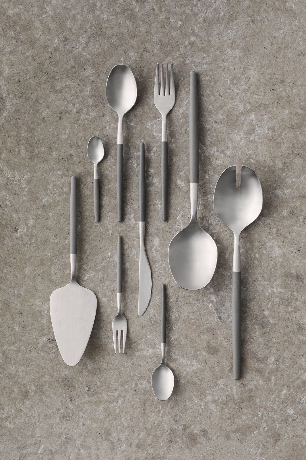 Modern stainless steel cutlery arranged on a textured gray surface.