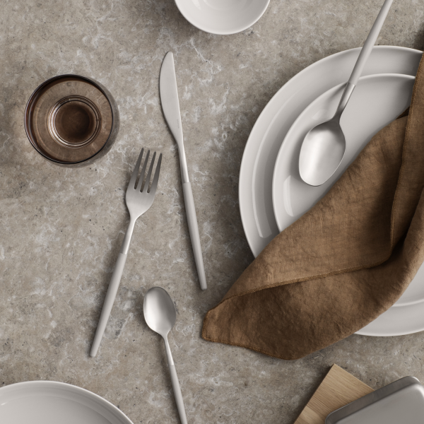 Elegant table setting with ceramic dishes, cutlery, and a linen napkin on a textured surface.