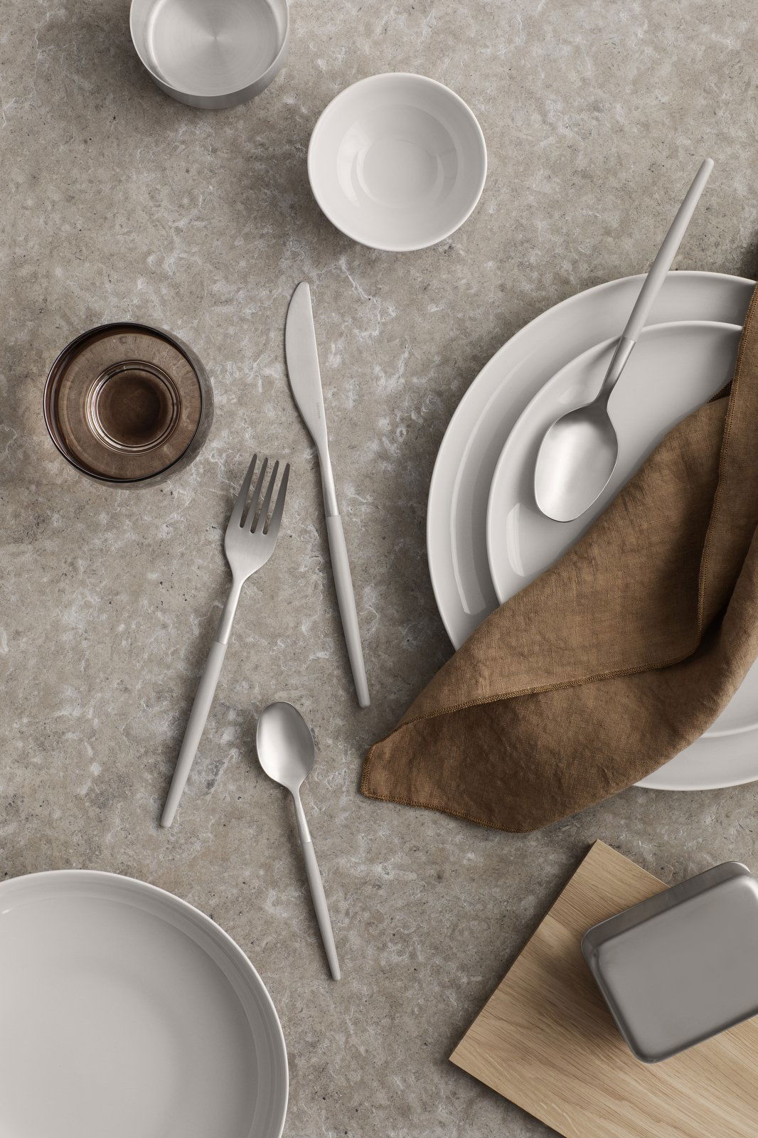 Elegant table setting with ceramic dishes, cutlery, and a linen napkin on a textured surface.