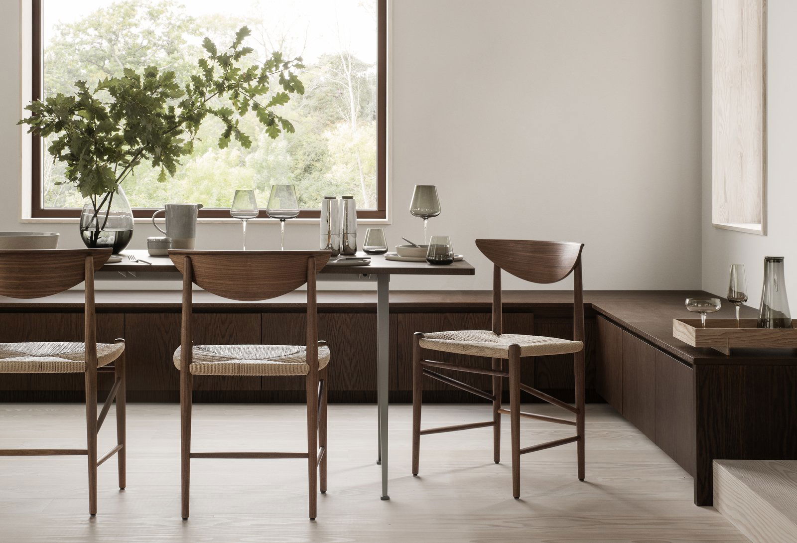 Modernes Esszimmer-Setup mit Holztischen und eleganten Gläsern in der Nähe eines großen Fensters.