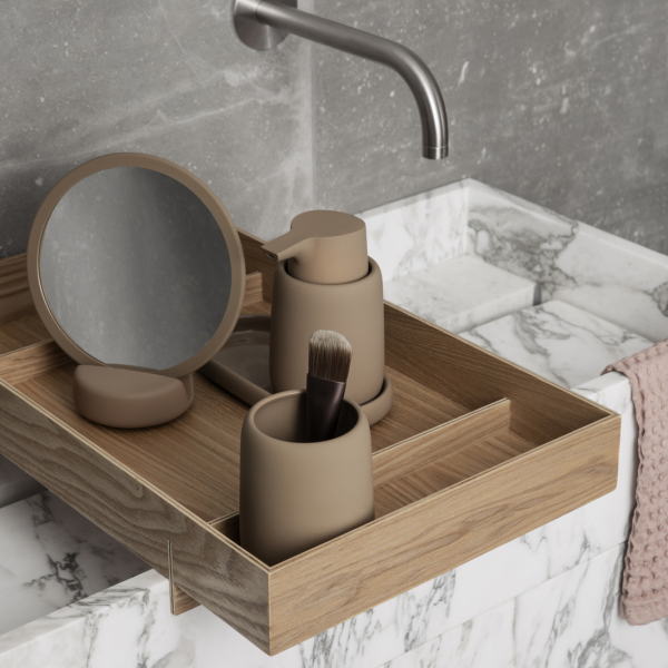 Elegant bathroom countertop setup with beige accessories and a round mirror on marble.