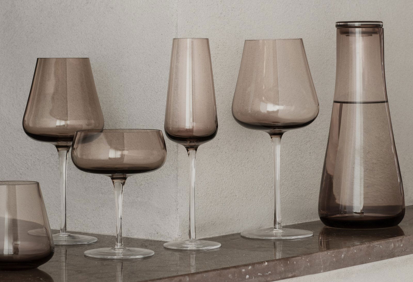 Elegant collection of smoky glassware displayed on a wooden shelf.