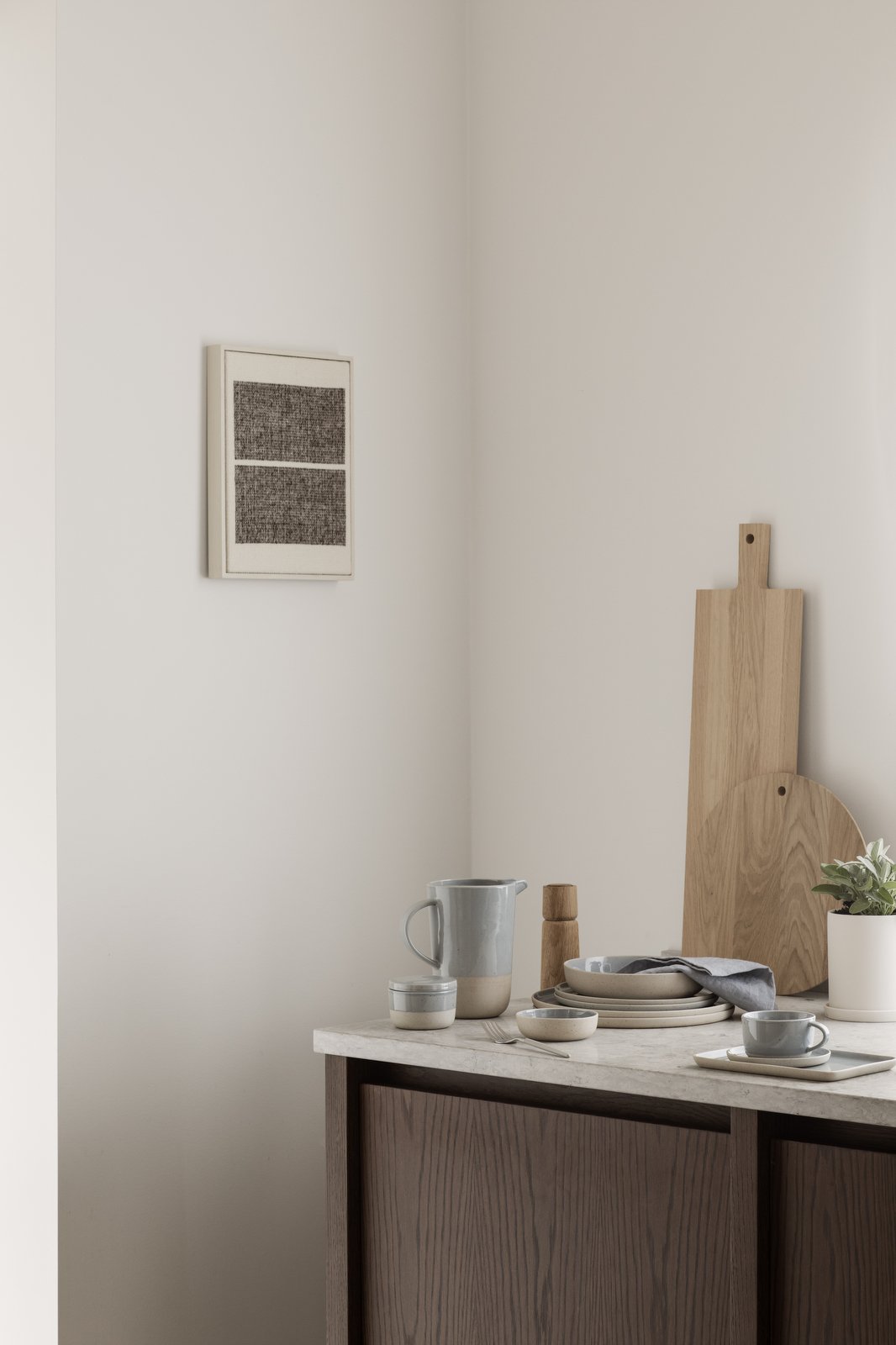Minimalist dining setup with tableware, a pitcher, and modern wall art in a serene space.