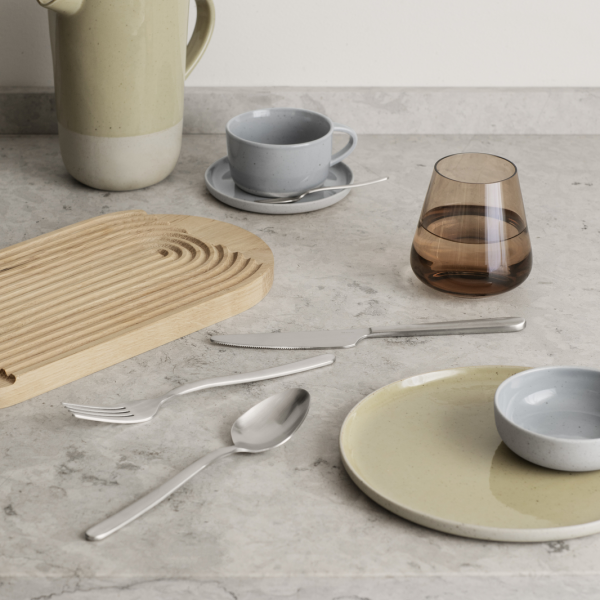 Stylish dining table setting with modern utensils, plates, and drinkware on a marble surface.