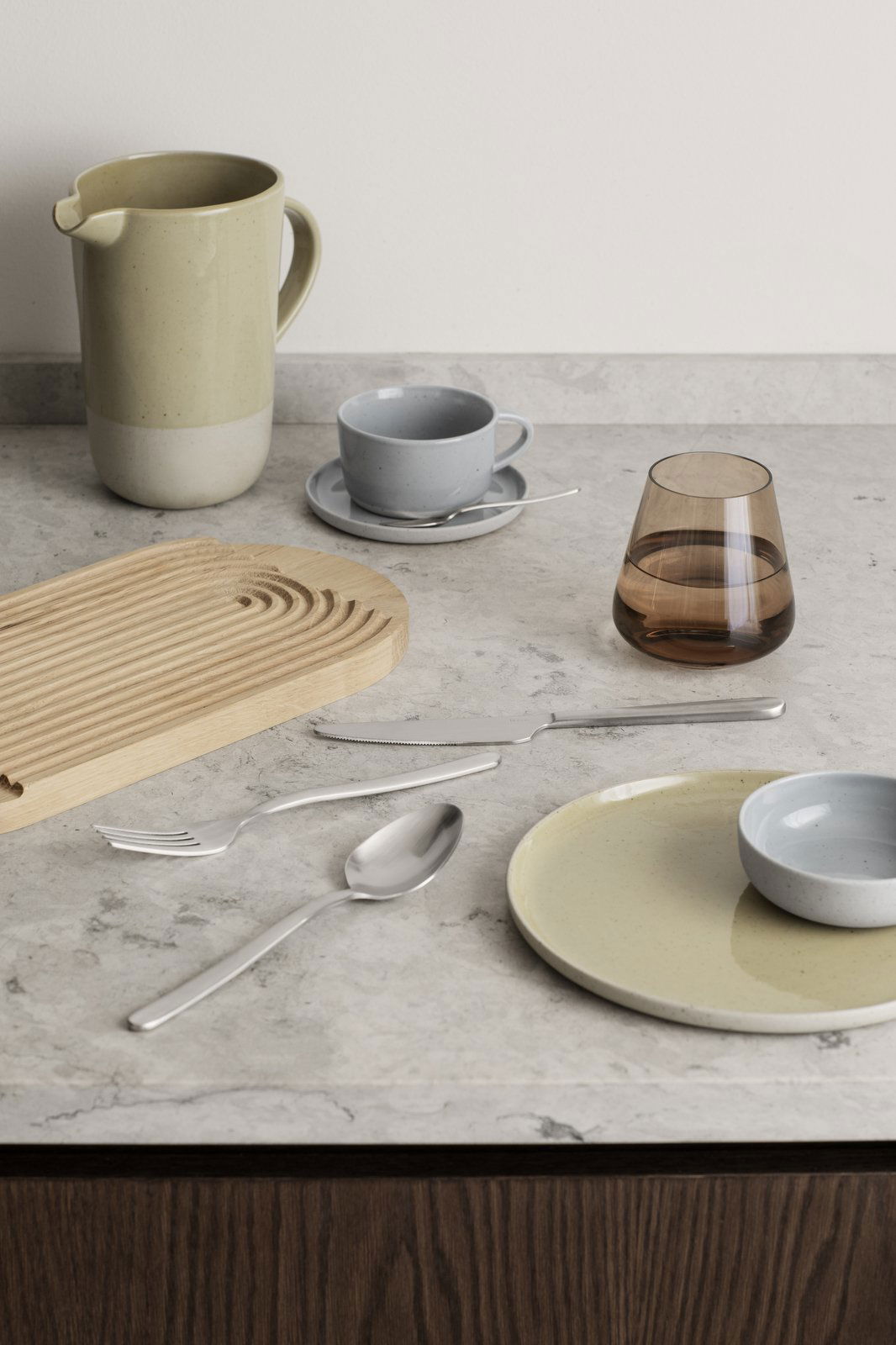Stylish dining table setting with modern utensils, plates, and drinkware on a marble surface.