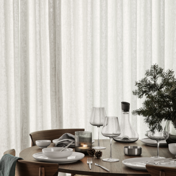Elegant dining table set with glassware, plates, and festive decor against soft curtains.