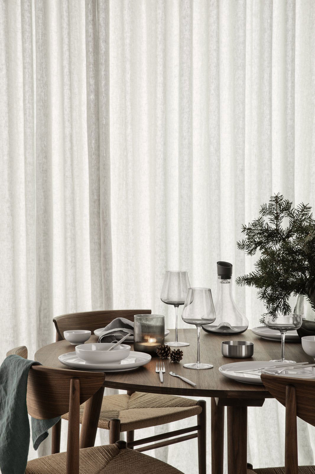 Elegant dining table set with glassware, plates, and festive decor against soft curtains.