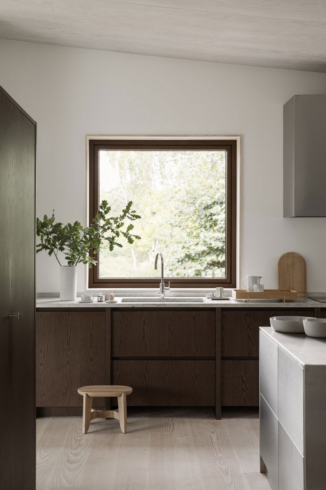 Moderne Küche mit Holzschränken, einem eleganten Spülbecken und einem großen Fenster, das ins Grüne blickt.