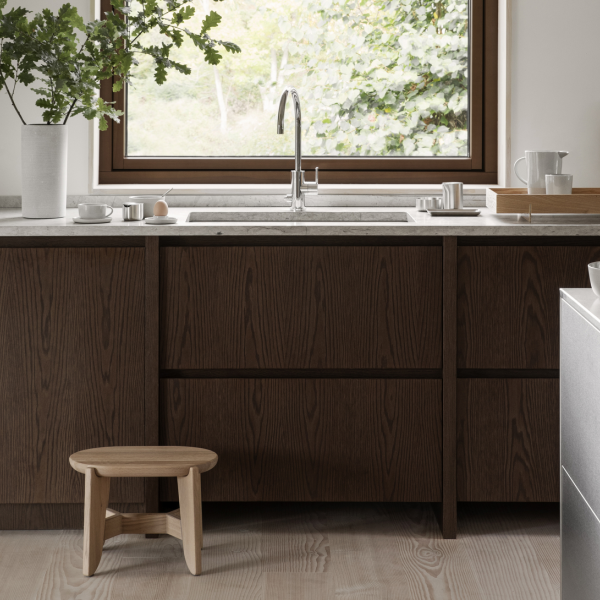 Modern kitchen with dark wood cabinets, a minimalist sink, and a wooden stool by the window.