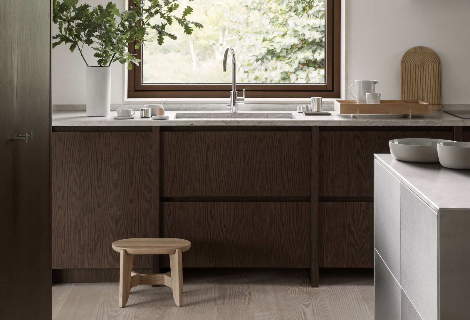 Modern kitchen with dark wood cabinets, a minimalist sink, and a wooden stool by the window.