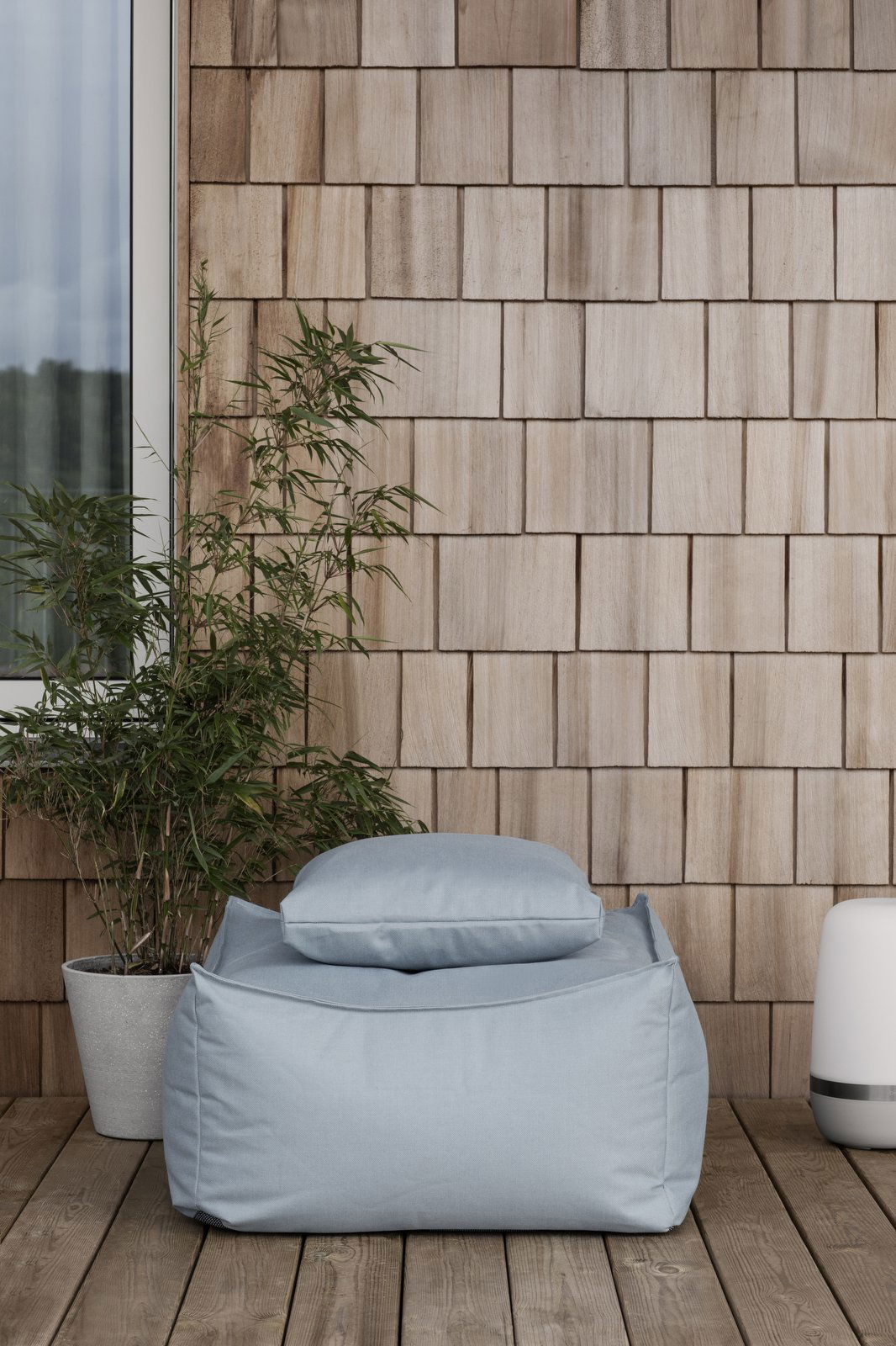 Cozy outdoor seating area with a bean bag, bamboo plant, and wooden wall backdrop.