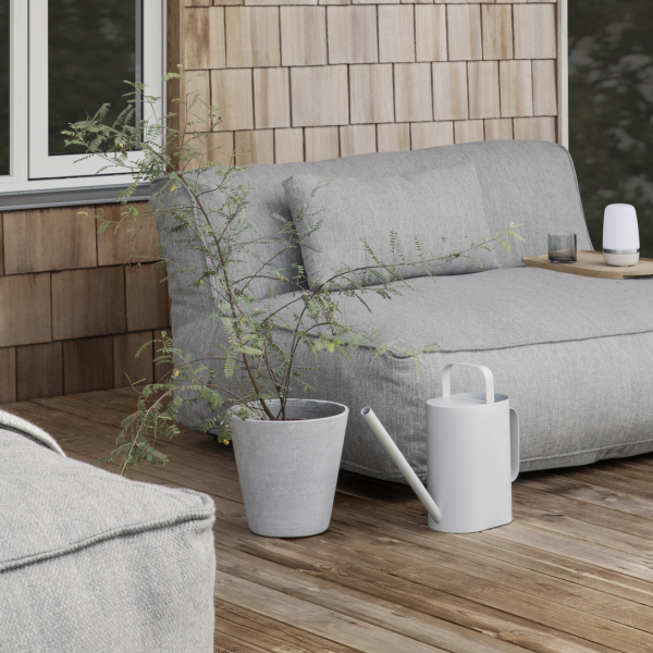 Gemütlicher Außenbereich mit einer grauen Couch, einer Pflanze und einer Gießkanne auf einer Holzterrasse.