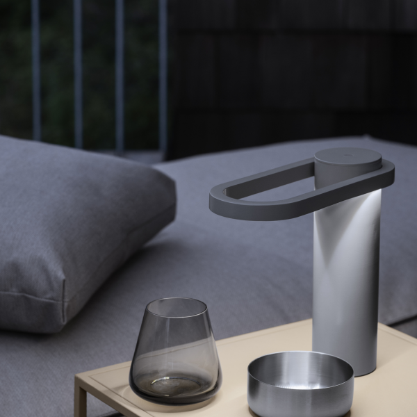 Stylische moderne Lampe auf einem Nachttisch neben einem Glas und einer Schüssel in einem gemütlichen Schlafzimmer.