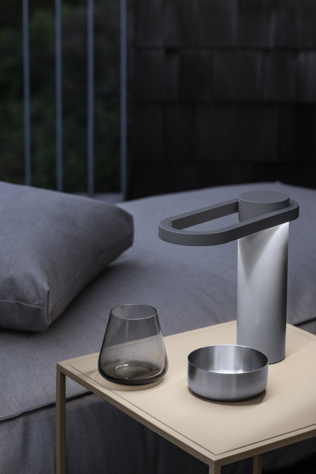 Stylische moderne Lampe auf einem Nachttisch neben einem Glas und einer Schüssel in einem gemütlichen Schlafzimmer.