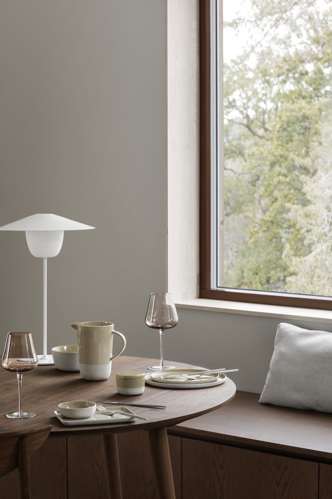 Elegantes Essgeschirr mit einer minimalistischen Lampe, Geschirr und einem Blick auf die Natur durch das Fenster.