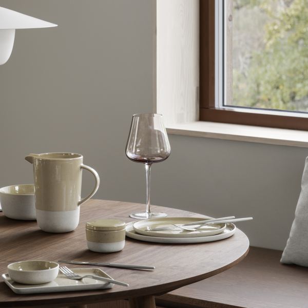 Stylish dining setup with ceramic tableware and a wine glass by a window.