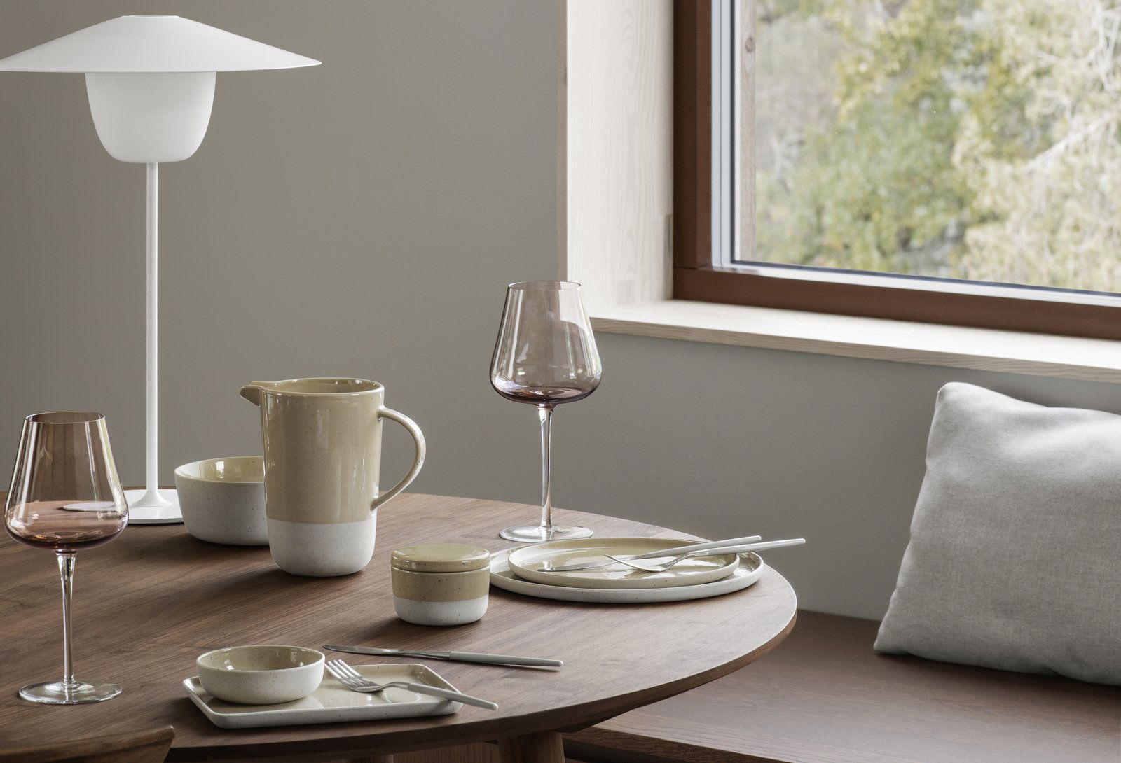 Stylish dining setup with ceramic tableware and a wine glass by a window.